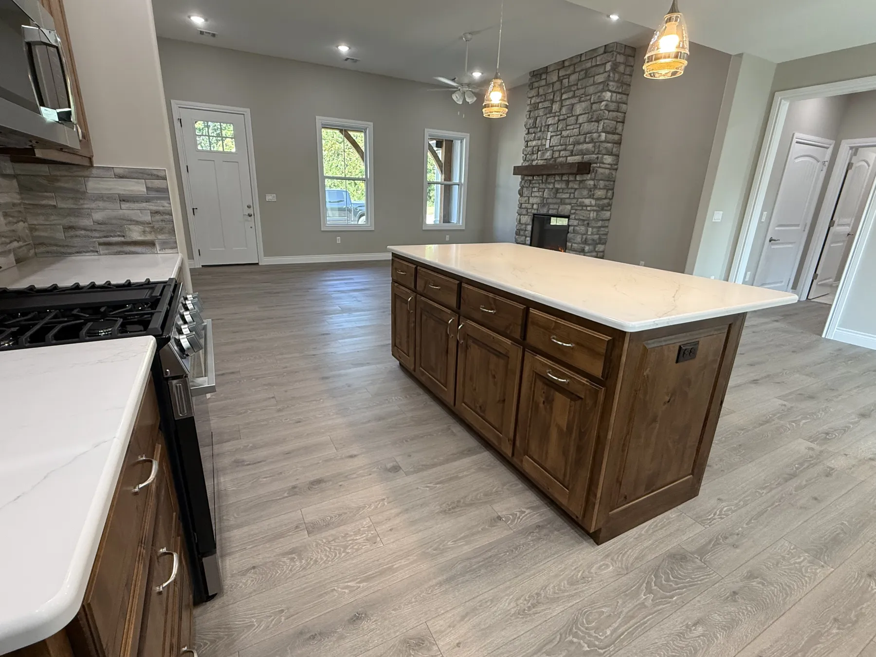 Open great room with a stacked stone fireplace, viewed past the kitchen island