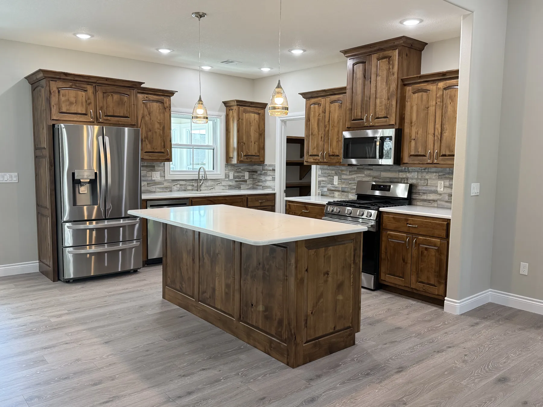 Kitchen with stained wood cabinets, quartz island, stainless appliances and pendant lights