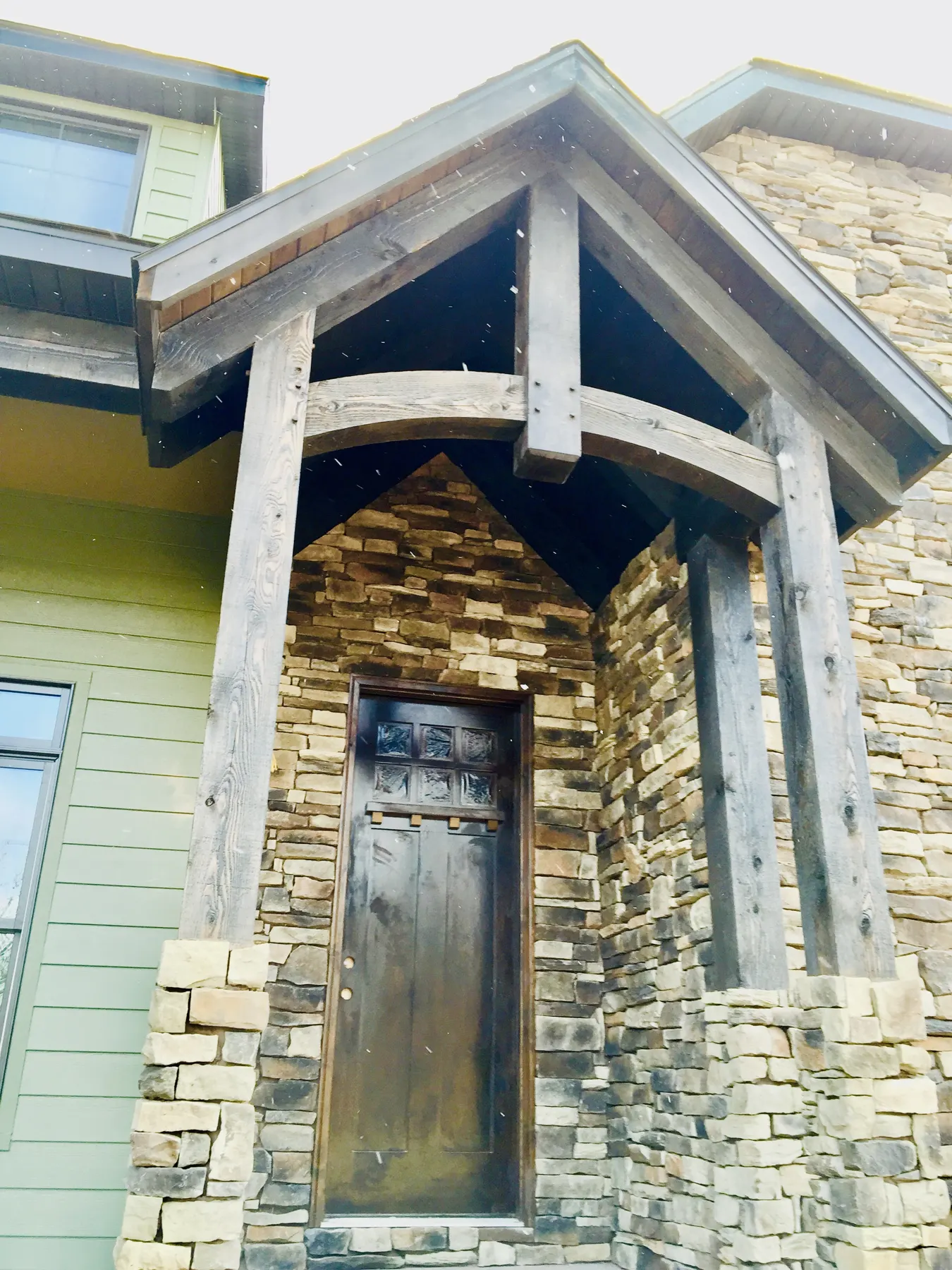 Timber-framed entry with a stone column and a dark wood front door