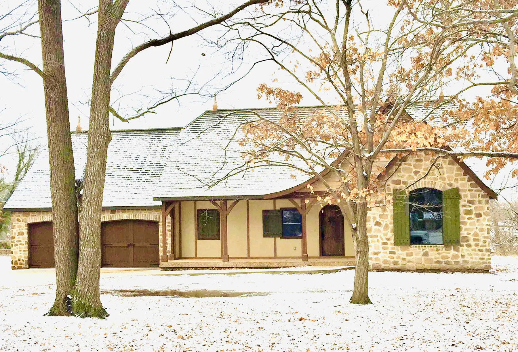 Stone and stucco home with a light snow on the yard