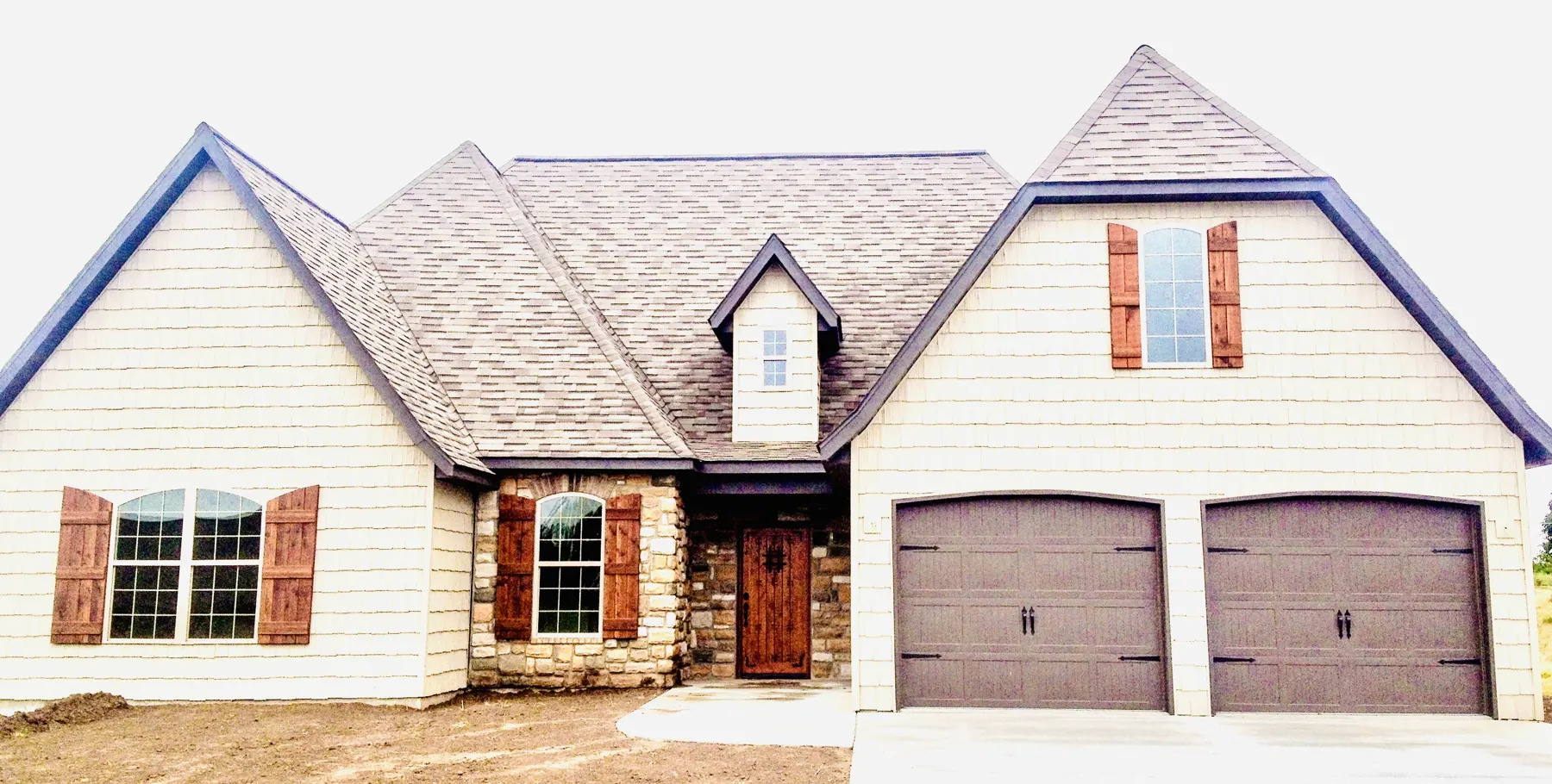 White home with brown shutters, a brick base and a two-car garage