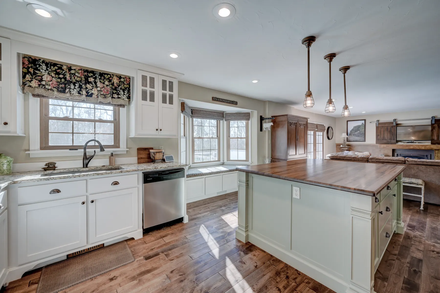 White kitchen with a farmhouse sink under the window and wood floors
