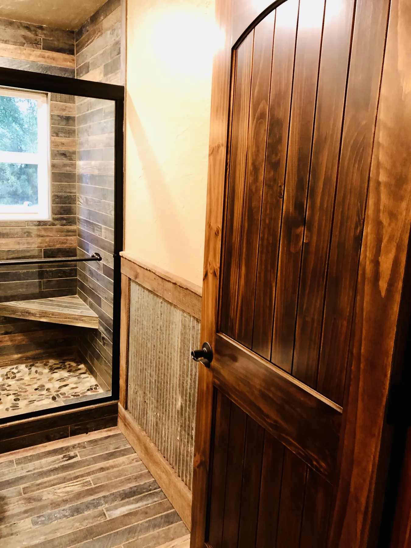 Bathroom with a plank wood door and wood-look tile shower
