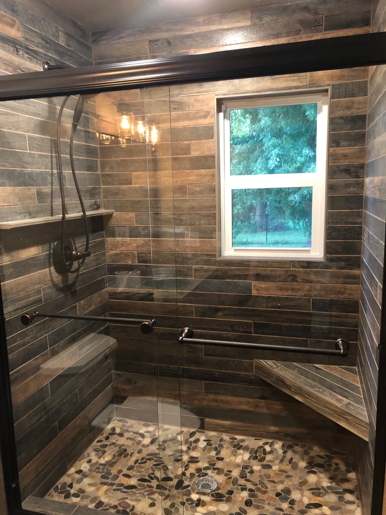 Shower with wood-look tile walls, a pebble floor and a window