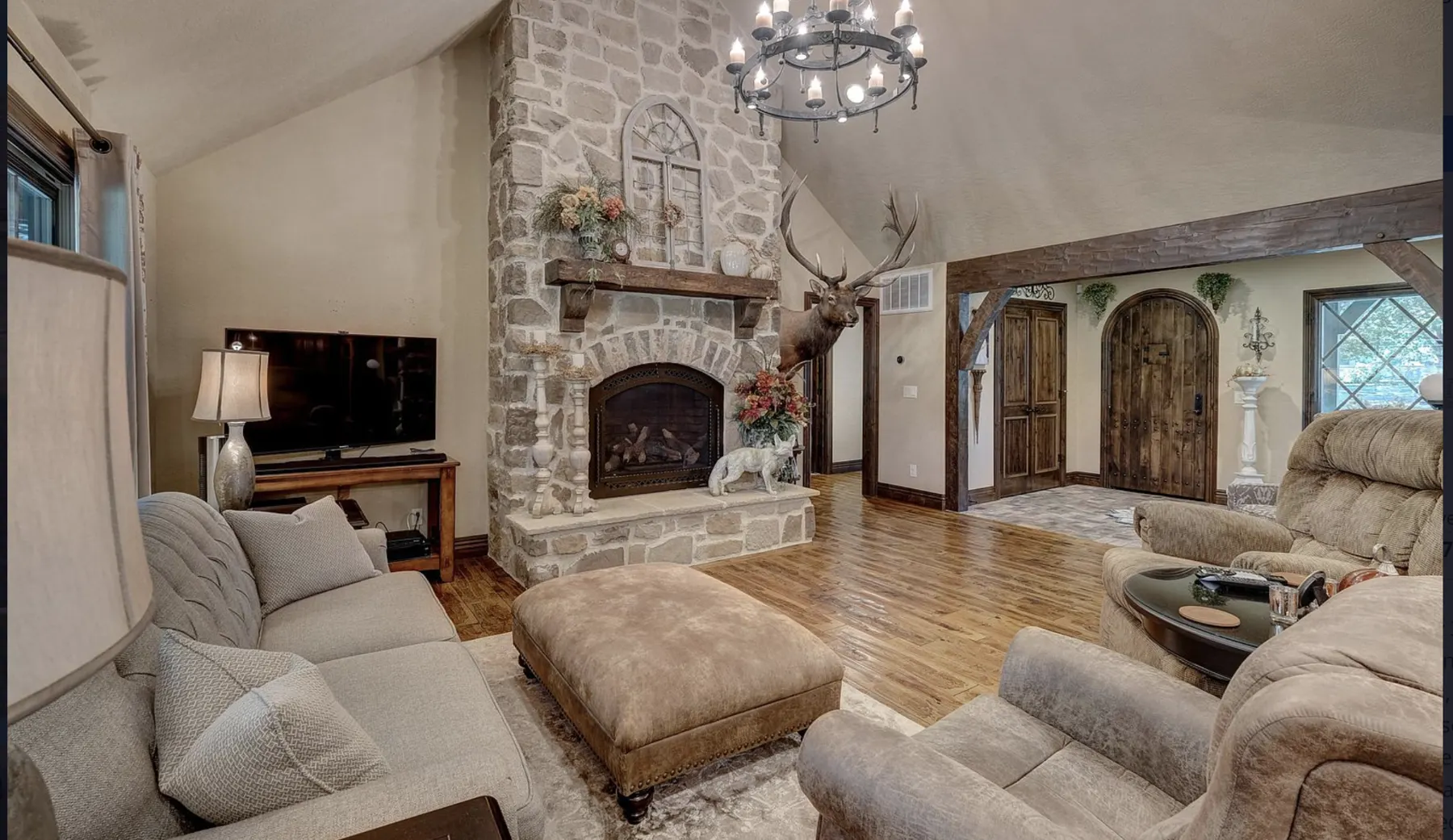 Great room with a floor-to-ceiling stone fireplace, wood floors and arched doorway