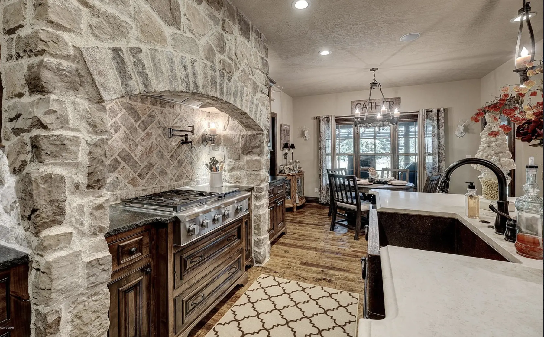 Kitchen with a stone range hood wall, dark cabinetry and white island