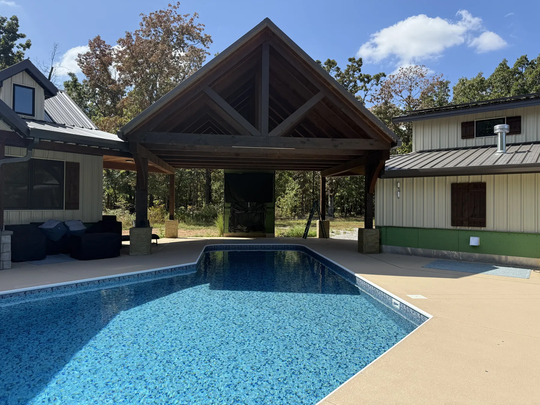 Timber-framed outdoor kitchen pavilion beside the pool, between the pool house and the shop