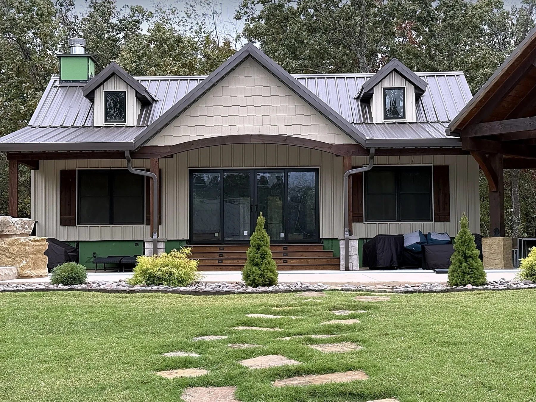 Front of the pool house with board and batten siding, dormers and wide glass doors, with a new lawn and stepping-stone path