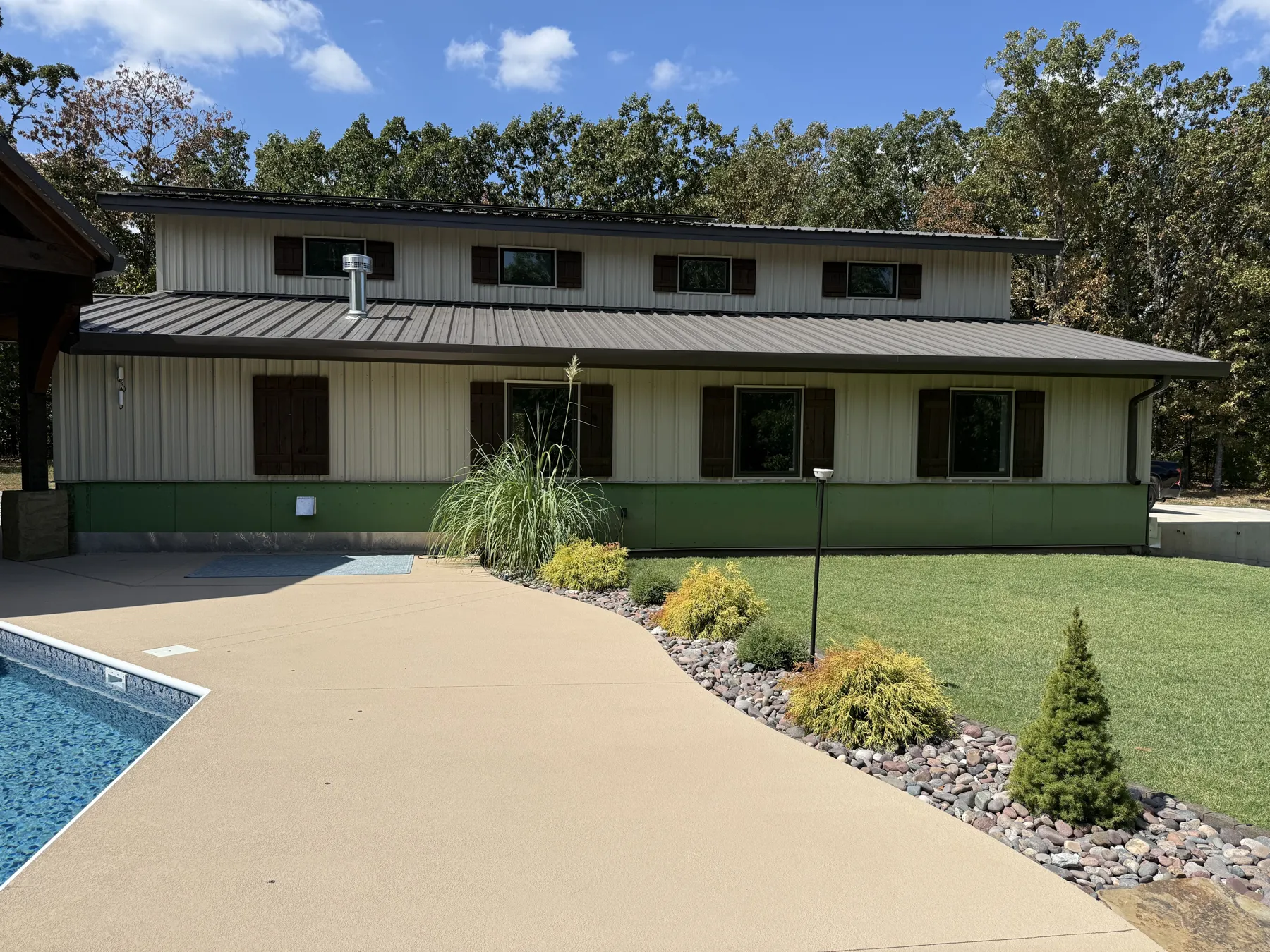 Two-story shop with metal roof and board and batten siding behind the pool deck and new landscaping